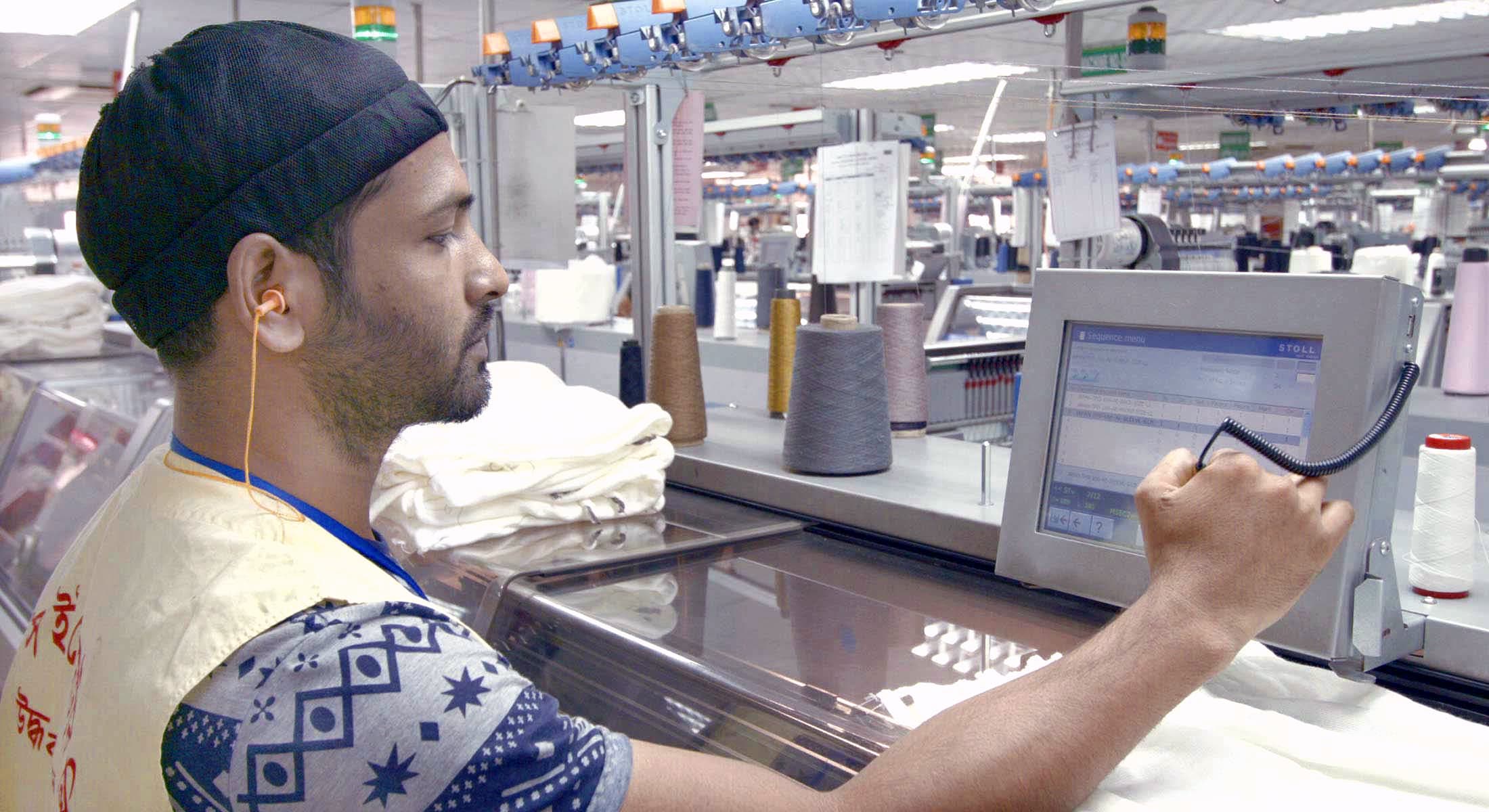 A knitting technician programming a Stoll flat-knitting machine